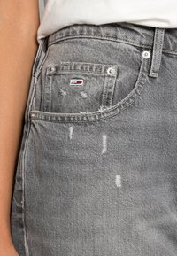 Dżinsy w jasnoszarym kolorze z postarzanymi detalami. Posiadają przednią kieszeń z małą naszywką z logo oraz metalowymi akcentami guzików.