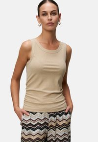 Débardeur beige à côtes avec un encolure large et une coupe ajustée, associé à un pantalon à motifs avec des designs en zigzag dans des tons terreux.