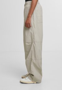 Beige cargo pants with an elastic waistband, wide-leg design, and side pocket. Worn with white and beige sneakers.