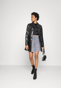 Jaqueta de couro preto brilhante, top preto justo e curto, saia xadrez azul e cinza, e botas de tornozelo pretas. Pequena bolsa preta como acessório.