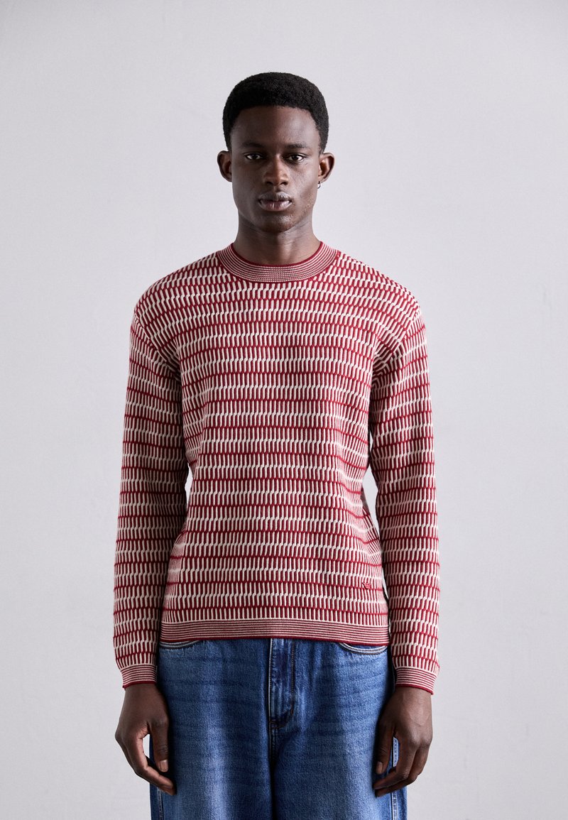 Pull à manches longues rouge et crème avec un motif, décolleté rond, en tissu tricoté, associé à un jean en denim ample.