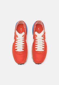 Red mesh and suede athletic shoes with white laces, blue accents on the heel, and a black rubber sole. Nike logo on the tongue.