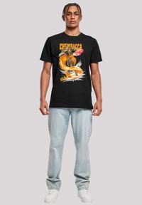 Juodas medvilninis marškinėliai su Chewbacca grafika, raudonais ir baltais akcentais, papildyti šviesiai mėlynomis džinsinėmis kelnėmis ir baltais sportiniais bateliais.