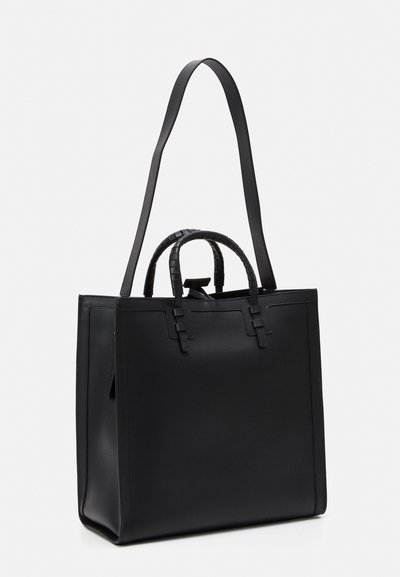 Sac fourre-tout en cuir noir avec une longue bandoulière et une poignée supérieure enroulée. Présente un design minimaliste et une forme carrée structurée.