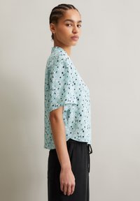Short-sleeve, light blue top with abstract black and white patterns, loose fit, soft texture, featuring a round neckline and side slits.