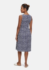 Marineblaues Kleid mit weißem abstraktem Muster, ärmelloses Design, taillierte Passform, ausgestellter Rock, Reißverschluss auf der Rückseite und flache Sandalen.