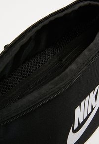 Sac noir Nike avec compartiment principal zippé ouvert, poche intérieure en mesh et logo Nike blanc visible à l'extérieur.