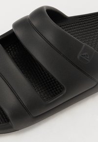 Sandale noire à bandeaux texturés en trois parties. Dispose d'un motif de tissages au niveau de la semelle et d'une légère contoured pour le confort. Matériau durable.