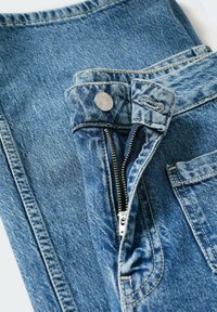 Jeans de mezclilla en azul claro, con un botón plateado, cierre de cremallera y un bolsillo frontal. La tela tiene una textura clásica con un ligero desvanecimiento.
