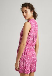 Bežėgrūdė rožinė šortai su sudėtingu baltu geometriniu raštu, su prigludusia liemene ir mažomis šoninėmis kišenėmis. Faktūrinis audinys.