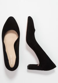 Pumps neri in suede con tacco alto e punta affusolata. Presentano un'apertura laterale e un'insole beige liscia.