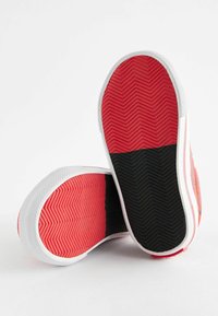 Semelle en caoutchouc rouge et noire avec motif en chevron et bord blanc ; les paires présentent des sections de couleurs contrastées ; texture lisse.