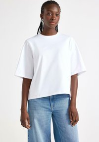 T-shirt bianco in cotone con una vestibilità rilassata, scollatura rotonda e maniche corte. Abbinato a jeans a gamba larga di un blu chiaro. La texture appare liscia.
