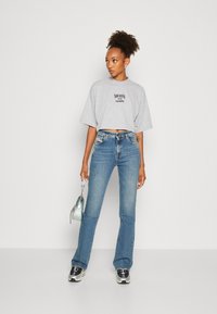 Gray cropped t-shirt with black print, high-waisted blue denim jeans, and sporty black and white sneakers. Holding a small iridescent bag.