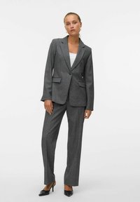 Pelēks piegriezts uzvalks ar vienas pogas žaketu un taisnām biksēm. Fakturēts audums, atlocāmie atloki un priekšējās kabatas. Melni augstpapēžu apavi.