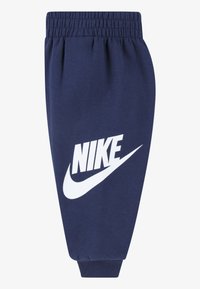 Pantaloni de trening bleumarin din material moale, cu talie elastică și un logo mare alb Nike pe partea din față. Design cu picior conic.