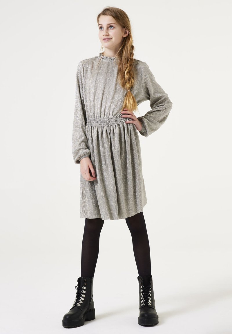 Robe à manches longues en ton argenté, avec un tissu texturé, une taille smockée et une jupe plissée, accompagnée de bottes de combat noires à lacets et de collants.