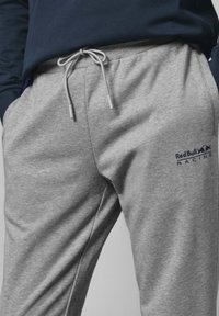 Grå sweatpants i mjukt material, med en justerbar dragkedja och en loggoprint av "Red Bull Racing" i blått.