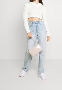 Virkad vit kort tröja med krage, högmidjade ljusblå jeans och en liten beige lackerad axelväska. Vita sneakers.