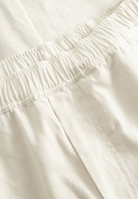 Gros plan sur un tissu blanc avec une ceinture élastique et des coutures visibles sur un vêtement.