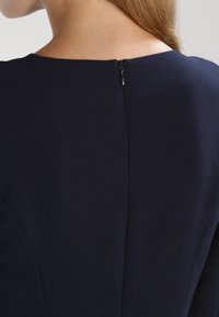 Námořnické šaty vyrobené z hladké tkaniny, se strukturovaným výstřihem a skrytým zadním zipem. Design je jednoduchý s minimem viditelných švů.