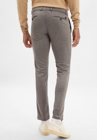 Pantaloni grigi slim-fit realizzati in tessuto testurizzato, con tasche posteriori con chiusura a bottone, abbinati a sneaker bianche e calzini alla caviglia.
