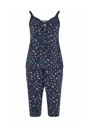 Mujer con cabello largo y castaño que lleva un top sin mangas y pantalones a juego con estampado floral y celestial azul oscuro, sobre un fondo claro y liso.