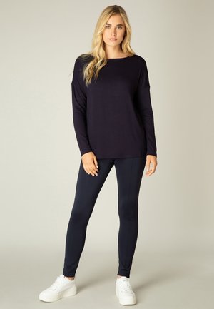 Marineblauw langemouwen top gecombineerd met strakke marineblauwe leggings en witte sneakers. Zacht, rekbaar materiaal met een ontspannen silhouet en ronde halslijn.