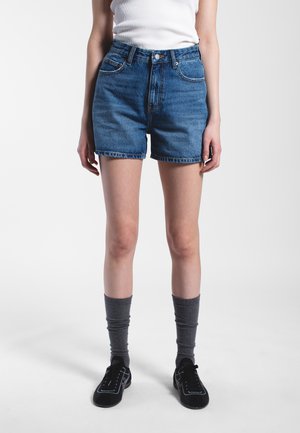 Denim shorts in medium blue featuring a high waist, five-pocket design, and frayed hem. Worn with gray knee-high socks and black shoes.