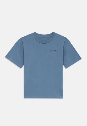 Mėlynas trumpomis rankovėmis marškinėliai su juodu mažuoju „Calvin Klein“ logotipu kairėje krūtinės pusėje, paprastas dizainas be kitų matomų detalių.