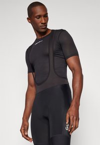 Melnas īsās velo bikses ar tīkla augšdaļu, īsām piedurknēm un pieguļošu dizainu. Smalki izšūšanas akcenti un logo uz kājas.