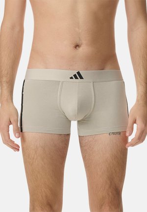 Boxer breves de algodón beige con rayas laterales negras, un ajuste ceñido y una cinturilla acanalada con el logo de Adidas en negro.