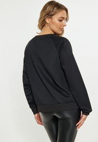 Felpa nera con vestibilità rilassata, maniche raglan e polsini a coste, realizzata in tessuto morbido. Leggings neri brillanti completano il look.