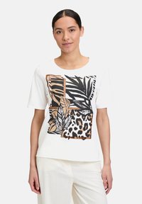 Weißes T-Shirt mit kurzen Ärmeln, das einen grafischen Druck von schwarzen Blättern, Leopardenflecken und braunen Akzenten in verschiedenen Formen und Texturen zeigt.