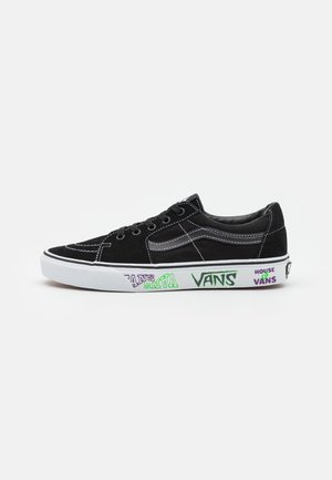 Zapatilla negra Vans de corte bajo con costuras blancas, suela blanca con logos de Vans en colores y texto "House of Vans" en el lateral.