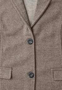 Veste en laine marron à motif chevrons, avec deux boutons noirs et poches en tissu assorti.