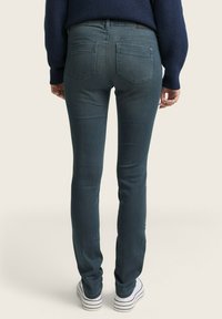 Sötétkék farmer skinny farmernadrág, közép derékkal és hátsó zsebekkel. Fehér csíkos sportcipővel viselve, kiemelve a formázott sziluettet.