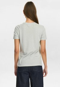 Tricou gri cu mânecă scurtă, cu un textură canelată, având un guler rotund și un design ajustat. Asortat cu pantaloni din denim închis.
