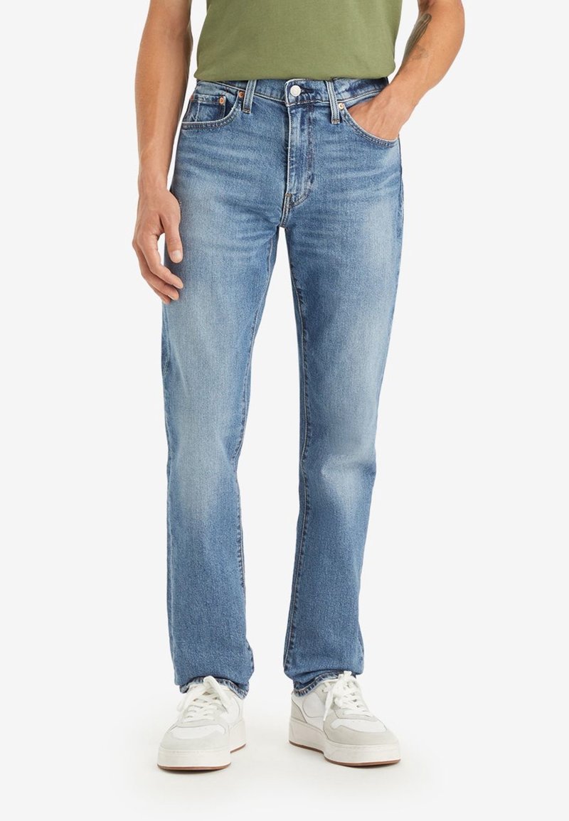 Ljusblå denimjeans med rak passform, blekt tyg, fem fickor och knapplåsning, kombinerade med vita sneakers.