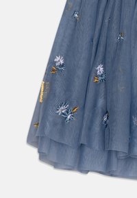 Niebieska spódnica z tiulu z kwiatowym haftem w pastelowych odcieniach, z złotymi akcentami i warstwowymi volanami, które dodają tekstury i wymiaru.