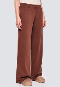 Brązowe szerokie spodnie dresowe z miękkiego materiału, z elastycznym pasem i kieszeniami bocznymi, w połączeniu z beżowymi butami typu slip-on.