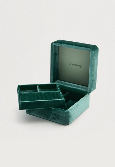 Πράσινο βελούδινο κουτί κοσμημάτων με αφαιρούμενο ένθετο που διαθέτει διαμερίσματα για δαχτυλίδια και μια λεία, επενδεδυμένη εσωτερική πλευρά με το όνομα της επωνυμίας στο εσωτερικό.