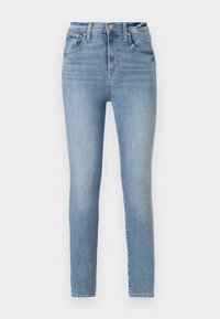 Vaqueros ajustados de tiro alto en azul claro con botón frontal, cremallera y diseño de cinco bolsillos sobre un fondo blanco liso.