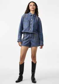 Denimist lõigatud jope, millel on kaks rinnataskut ja frantsi detail, koos denim lühikeste pükstega. Mustad põlvikud saabastega lõpetavad komplekti.