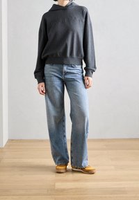 Sudadera con capucha de color gris oscuro con texto bordado, combinada con jeans de pierna ancha de color azul claro y zapatillas de color beige. Tejido suave y corte relajado.