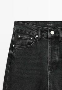 Jeans in denim neri con taglio dritto, caratterizzati da finiture in metallo argentato, design a cinque tasche e una trama testurizzata. L'etichetta riporta "Massimo Dutti."