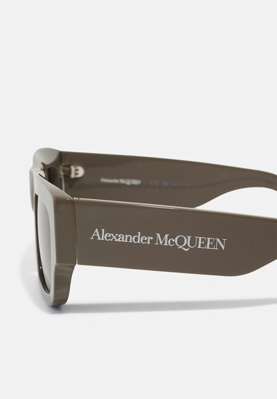 Ochelari de soare din plastic maro, cu rame groase, având un finisaj mat și logo-ul "Alexander McQueen" pe margine. Lentile întunecate.