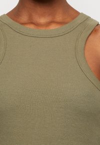 Olive green ribbed tank top with wide neckline and sleeveless design. Features a textured fabric and subtle stitching details.