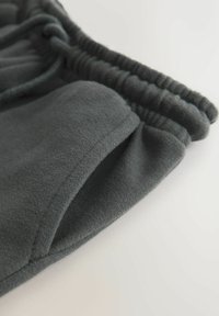 Temno sive trenirke s mehko teksturo, elastičnim pasom in stranskim žepom. Tkanina je videti gladka s priložnostnim dizajnom.