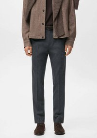 Szare spodnie z mieszanki wełny o prostym kroju z subtelnymi prążkami. Połączone z brązowym swetrem rozpinanym na guziki i ciemnobrązowymi butami.